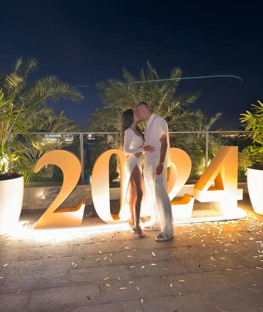 Couple kissing in front of illuminated 2024 sign.