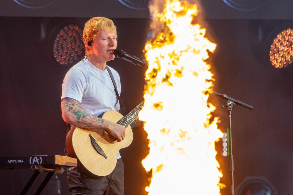 Ed Sheeran performing at a concert with a fire display.