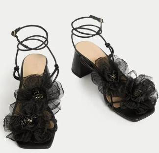 Black block heel sandals with black flower accents and ankle ties.