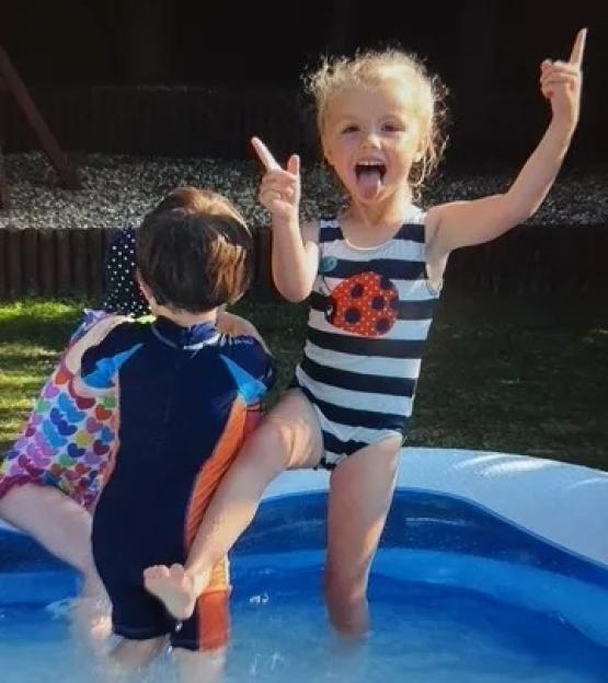 Two young children playing in a paddling pool.