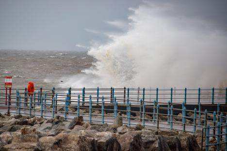 Strong onshore winds causing large waves to crash over a breakwater.