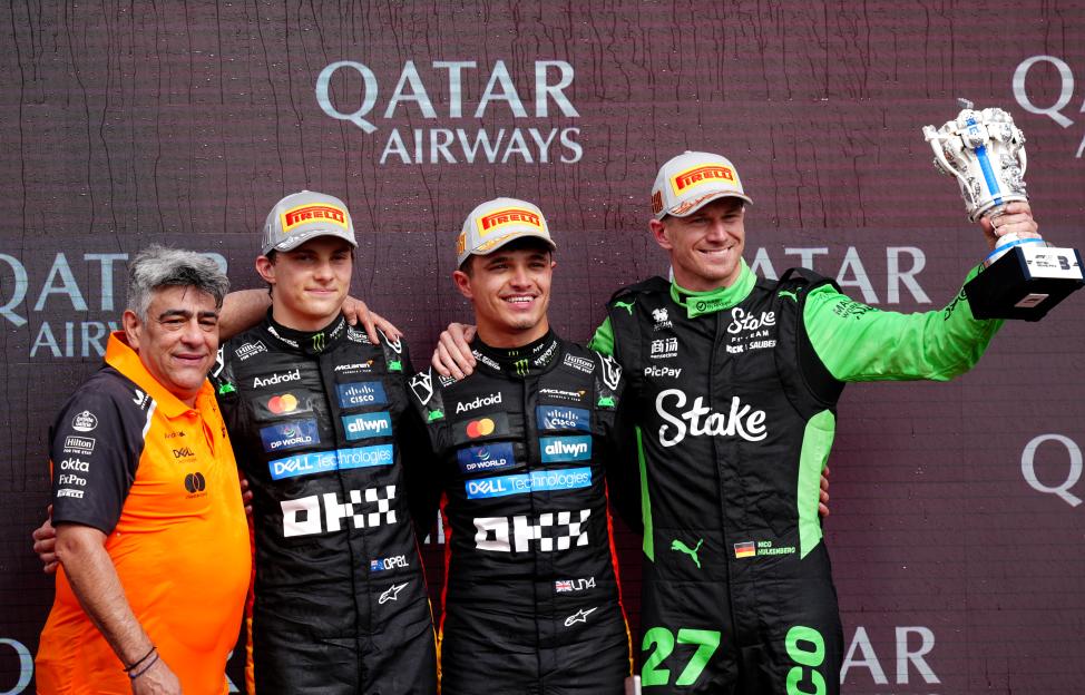 Three Formula 1 drivers on a podium, one holding a trophy.