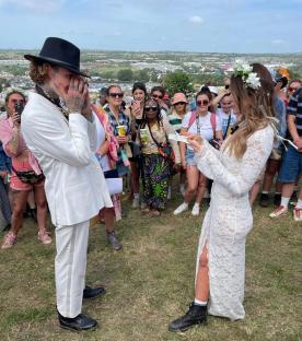 A couple exchanging vows at Glastonbury Festival, surrounded by cheering onlookers.