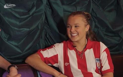 JoJo Siwa smiling while wearing a red and white striped shirt.