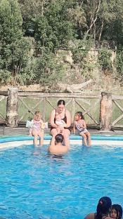 Woman and three children sitting at the edge of a pool.