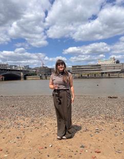 Woman holding a glass of wine standing on a beach with a city skyline in the background.