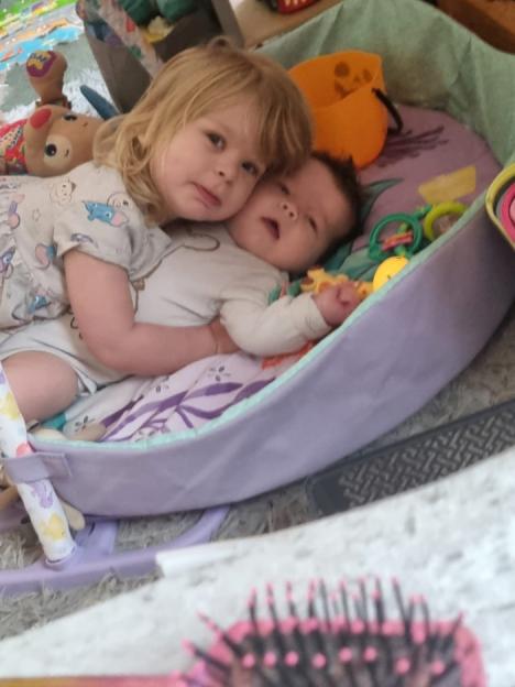 Toddler hugging a baby in a playmat.