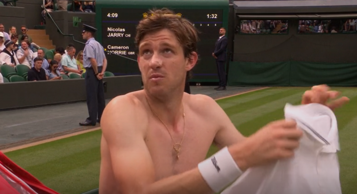 Shirtless tennis player putting on his shirt.