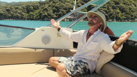 Noel Edmonds on a boat, arms outstretched.