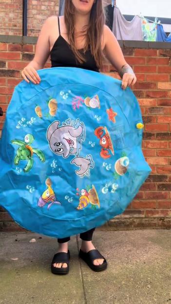 Person holding up a blue inflatable children's paddling pool with sea creatures printed on it.