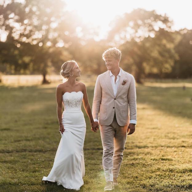 Bride and groom walking hand-in-hand in a field at sunset.