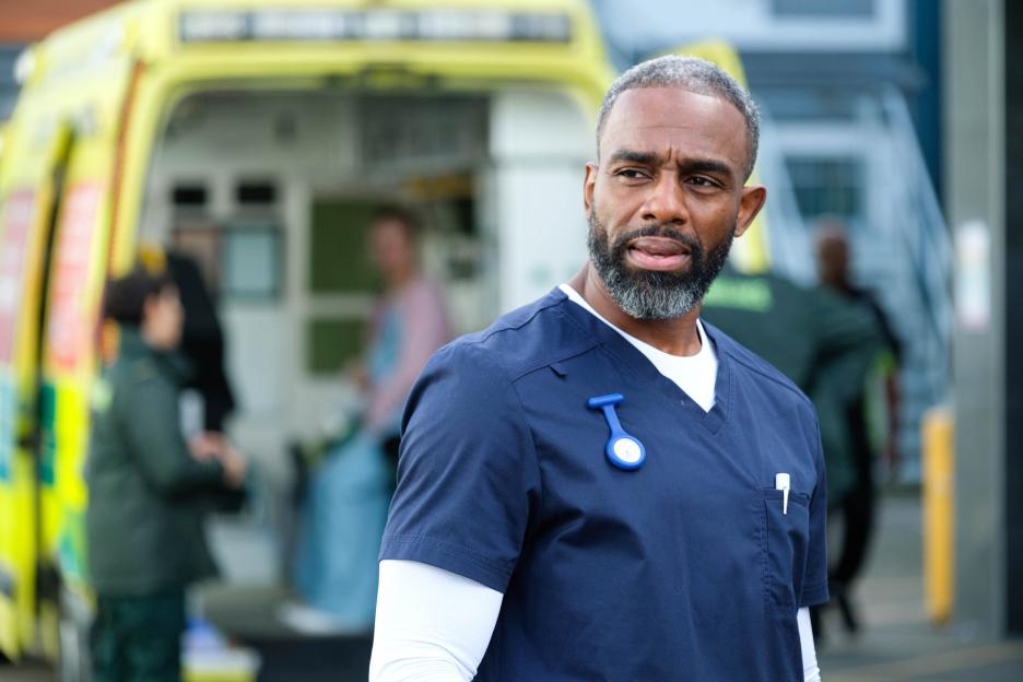 A male nurse stands outside an ambulance.