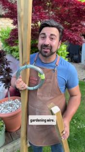 Man holding gardening wire and wooden post.