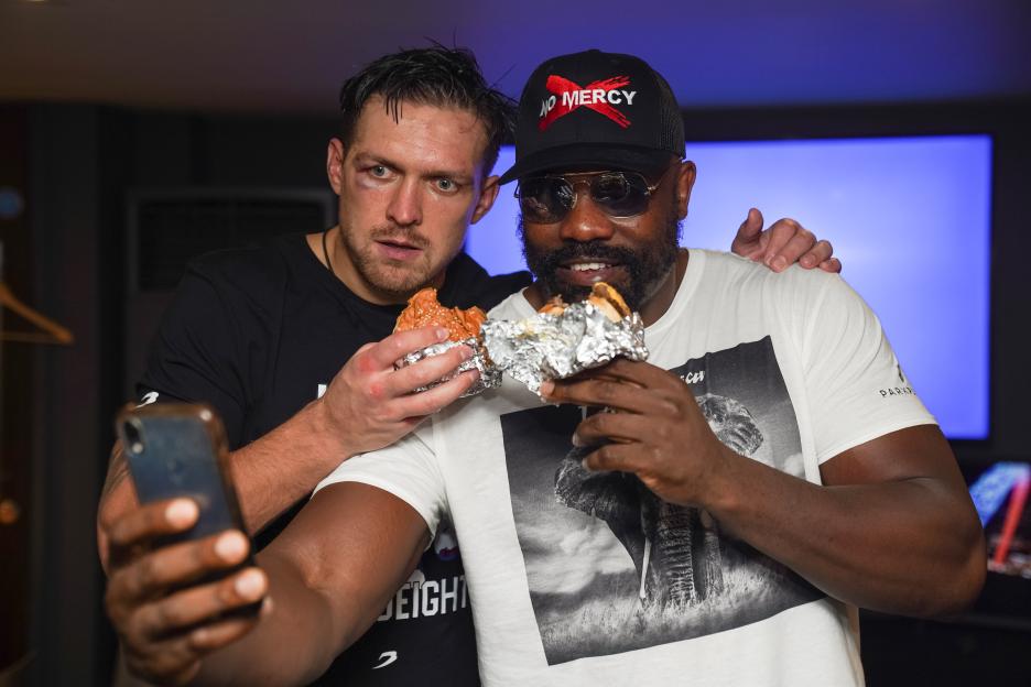Two boxers sharing a burger and taking a selfie.