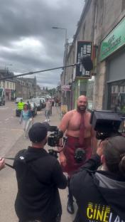 Tyson Fury in a kilt and tie, being filmed on a street.