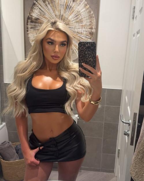 Selfie of a blonde woman in a black crop top and mini skirt.