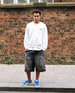 Man in white sweatshirt and denim shorts wearing blue Adidas sneakers.