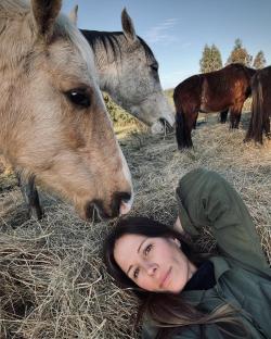 Woman lying in hay with horses.