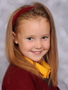 Portrait of a girl with long hair wearing a maroon cardigan and a yellow collared shirt.