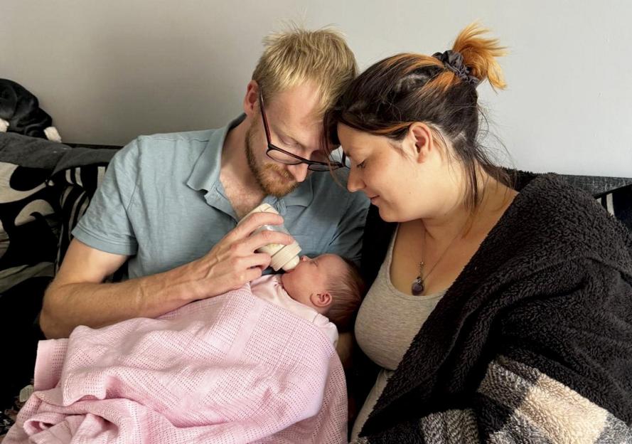 A mother and father bottle-feeding their newborn baby.