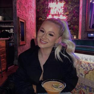 Photo of a young woman smiling and holding a cocktail.