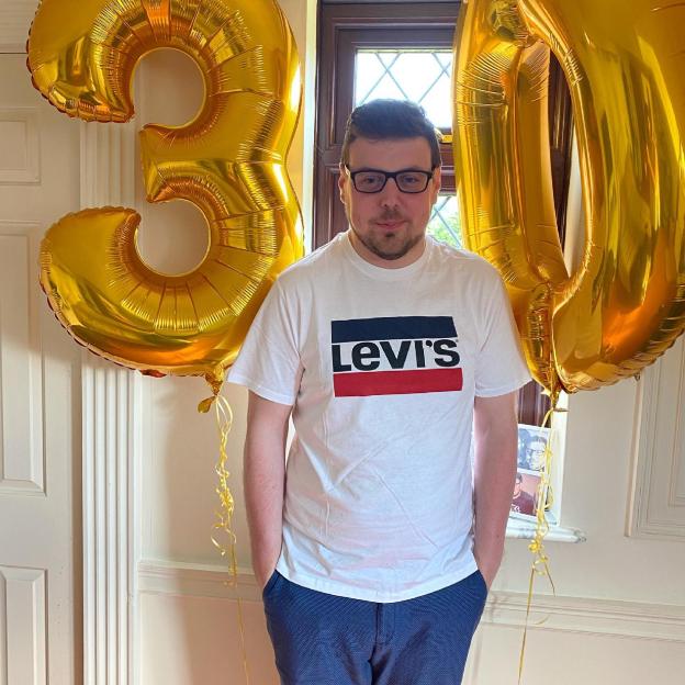 Man in Levi's t-shirt standing between two large gold number 30 balloons.