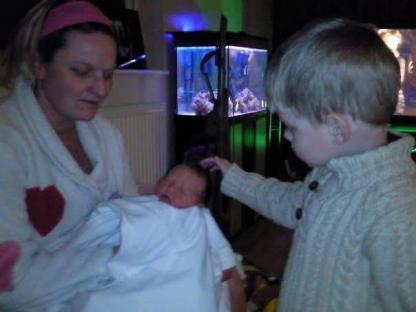 Woman holding a baby while a young boy looks on.