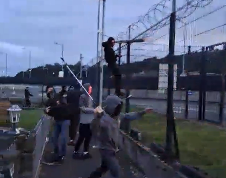 People firing fireworks over a fence.