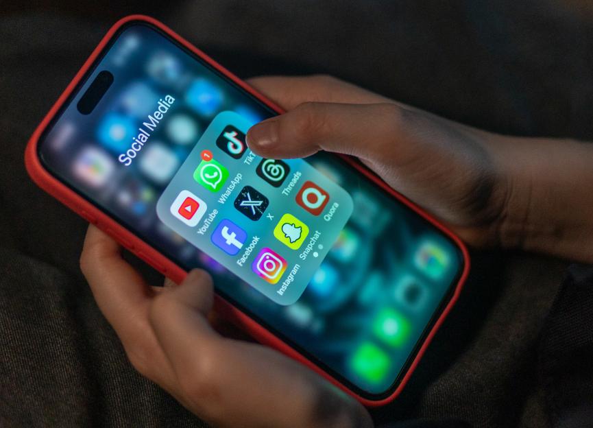 A child's hands holding a phone displaying various social media apps.