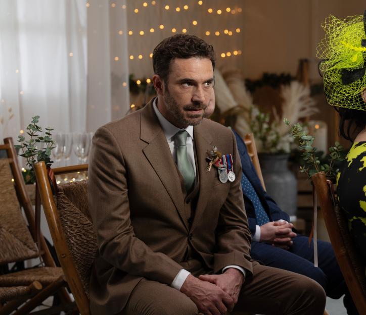 Man in brown suit at a wedding, wearing medals.