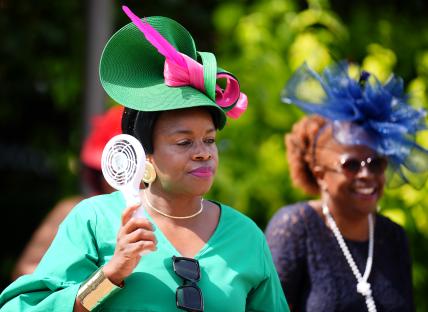 Woman at a horse race uses a handheld fan.