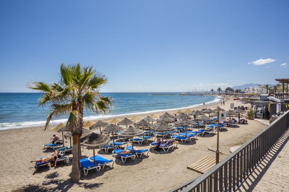 Beach scene in Marbella, Spain, with beach umbrellas and lounge chairs.