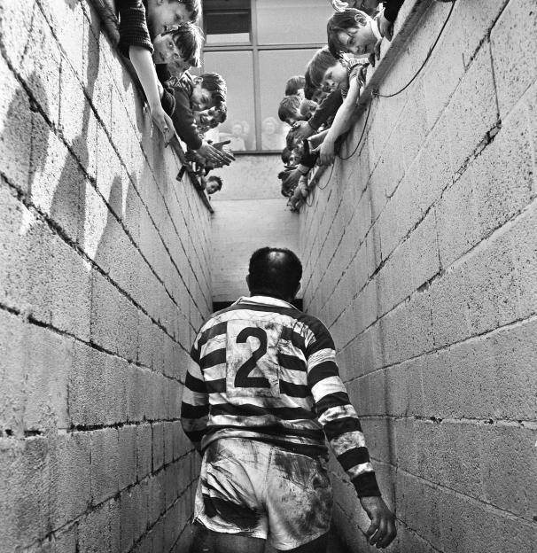 Billy Boston, wearing a rugby jersey, walks through a tunnel while children cheer.