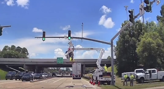 Workers repairing traffic lights on a highway overpass.
