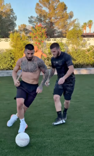 Two shirtless men playing soccer on a lawn.
