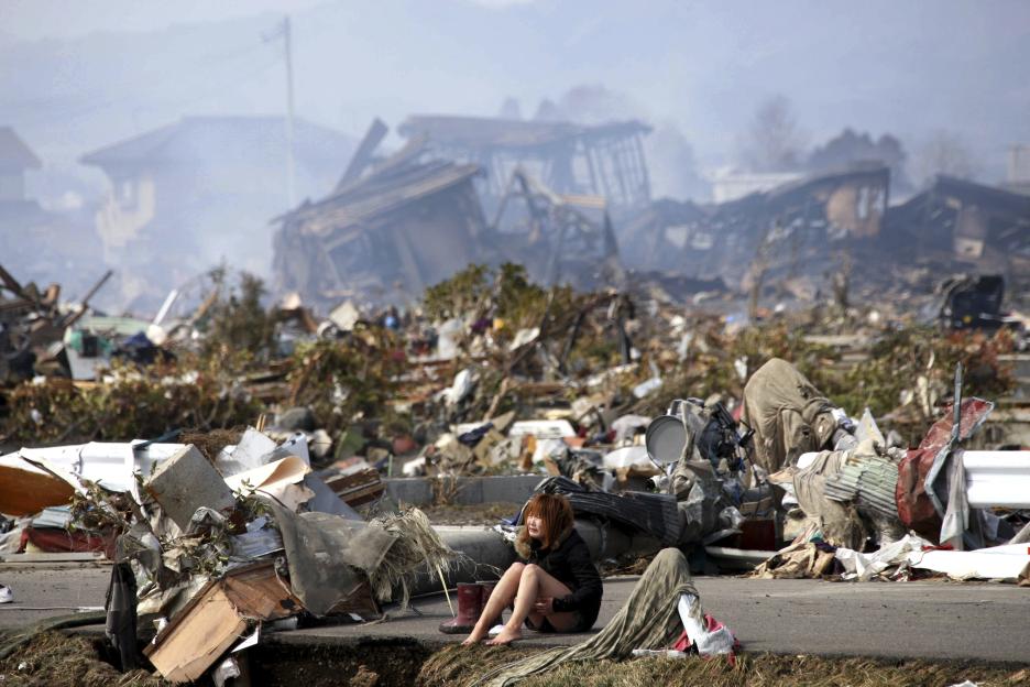 A woman sits amidst debris in the aftermath of a tsunami.