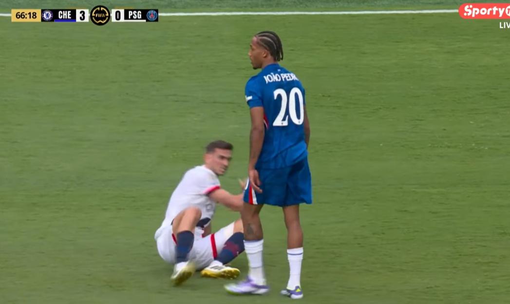 Soccer player falling on the field while another player looks on.