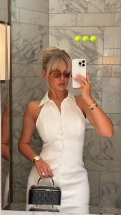 Woman in white dress taking a selfie in a bathroom.
