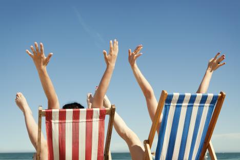 Two women relaxing in beach chairs with their arms raised in the air.
