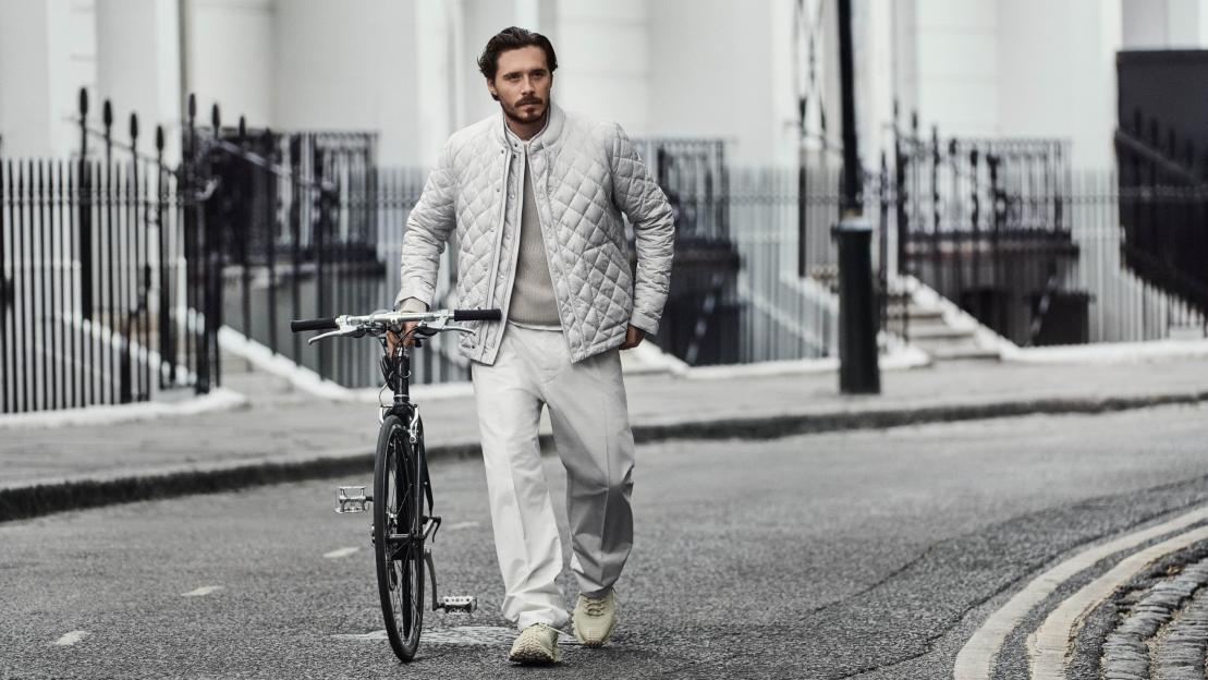 Man in Moncler Pre-Fall 2025 collection walking with bicycle.