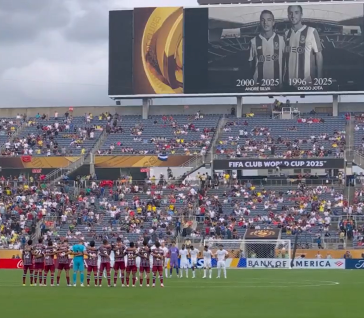 Soccer players standing on a field in front of a large stadium crowd.