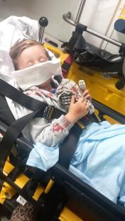 Child with blood on his face and clothing lying on a stretcher.