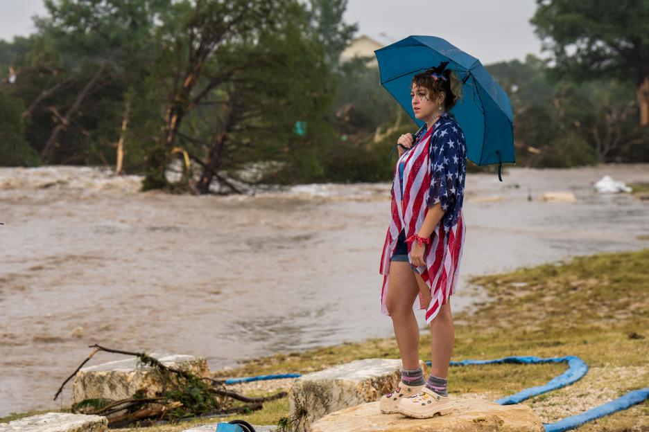 Woman under umbrella watching floodwaters.