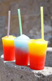 Three colorful slushy ice drinks in plastic cups.
