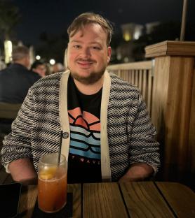 Man sitting at an outdoor table with a drink.