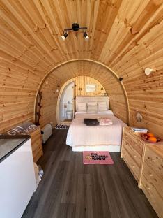 Interior view of a wooden cabin bedroom with a bed, dresser, and small bathroom.