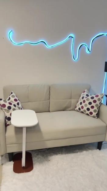 Beige sofa with side table and patterned pillows against a wall with blue LED lights.