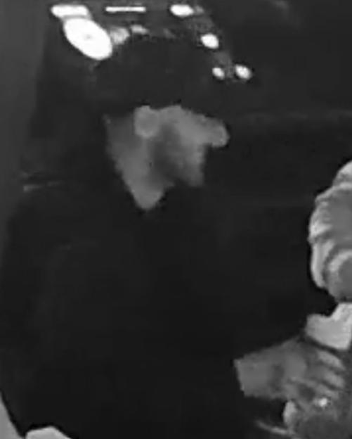 Low-quality security camera image of a person wearing a hat and dark clothing.