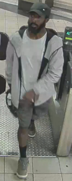 Surveillance image of a man wearing a gray jacket, white shirt, gray shorts, and gray shoes.