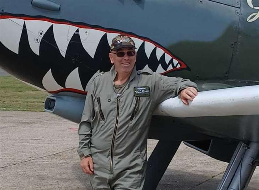 Man in flight suit leaning on a World War II airplane.